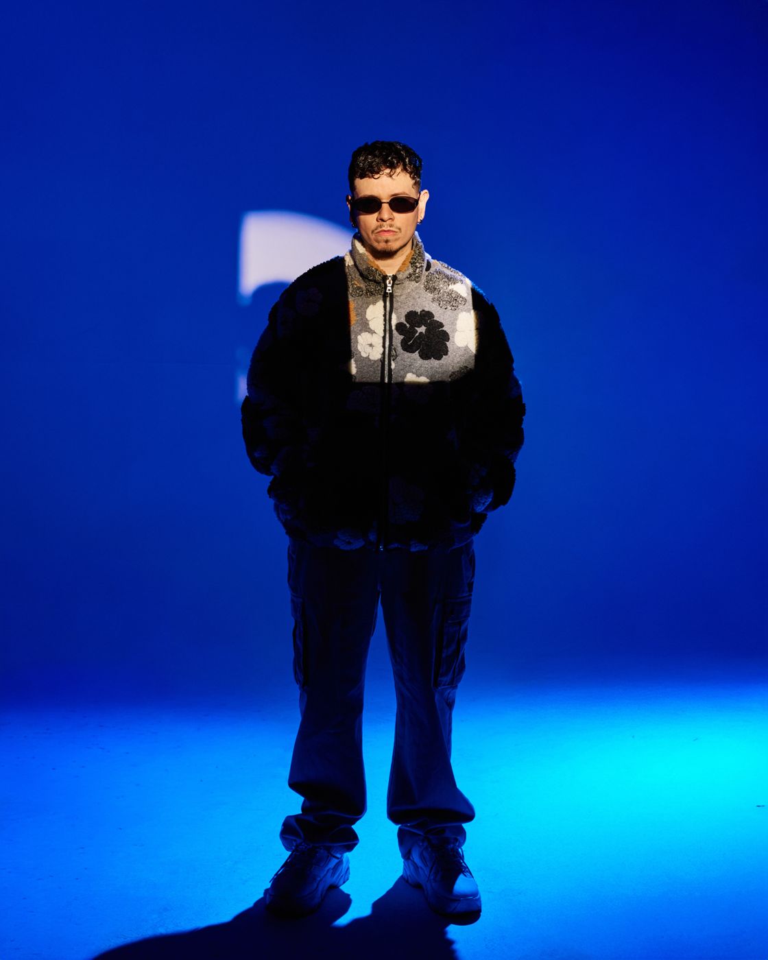 Man in sunglasses and a graphic jacket under saturated blue light