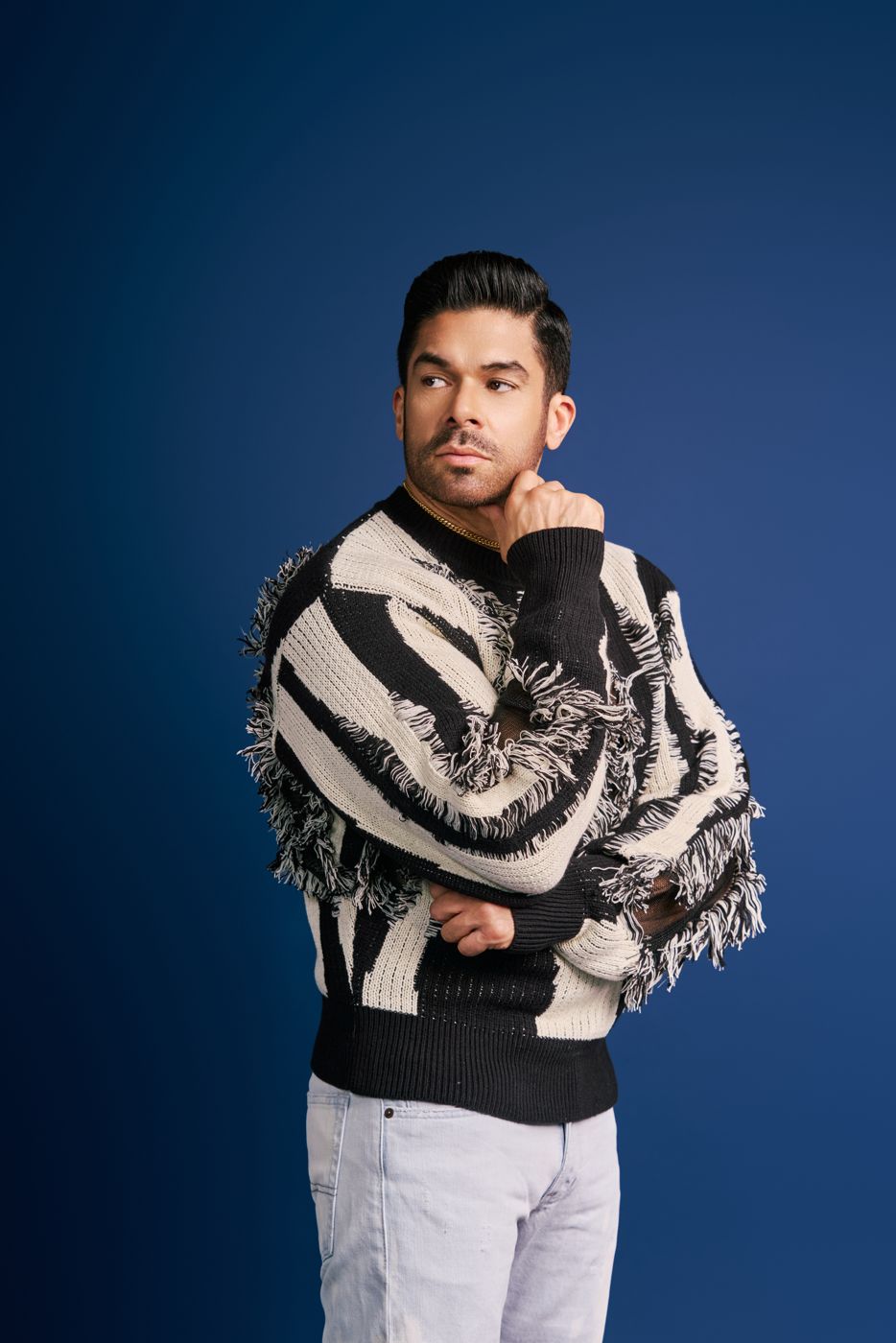 Man in a black and white fringe sweater against a deep blue backdrop