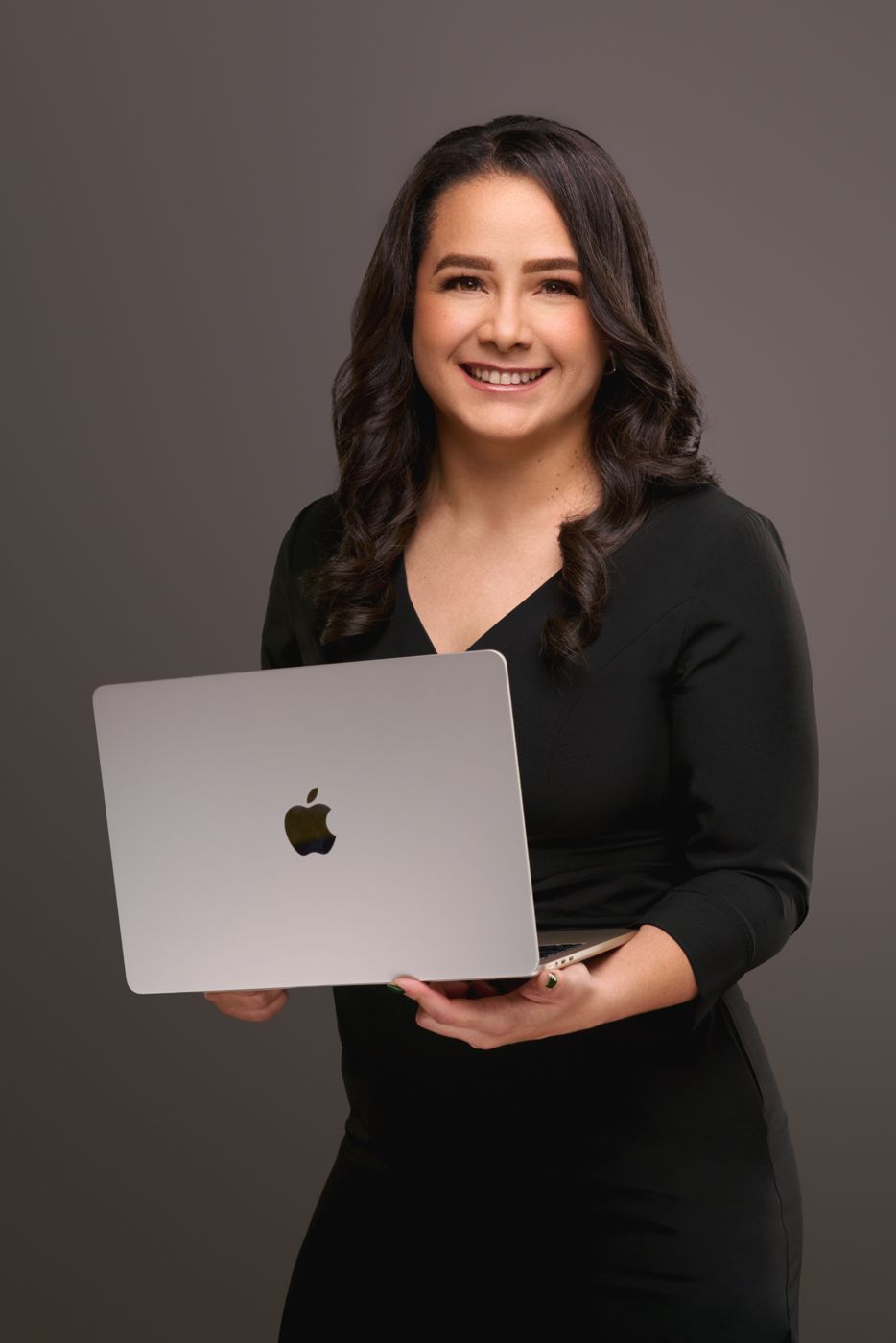 Professional in black holding a laptop against a grey studio backdrop