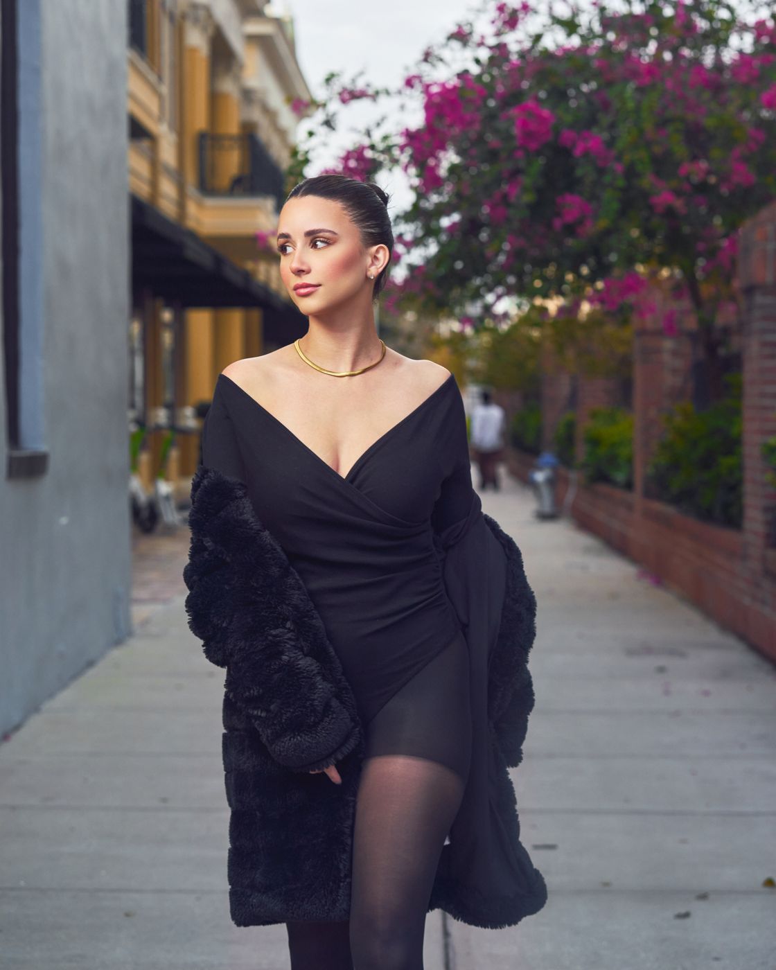 Woman in a black coat walking down a flower-lined street