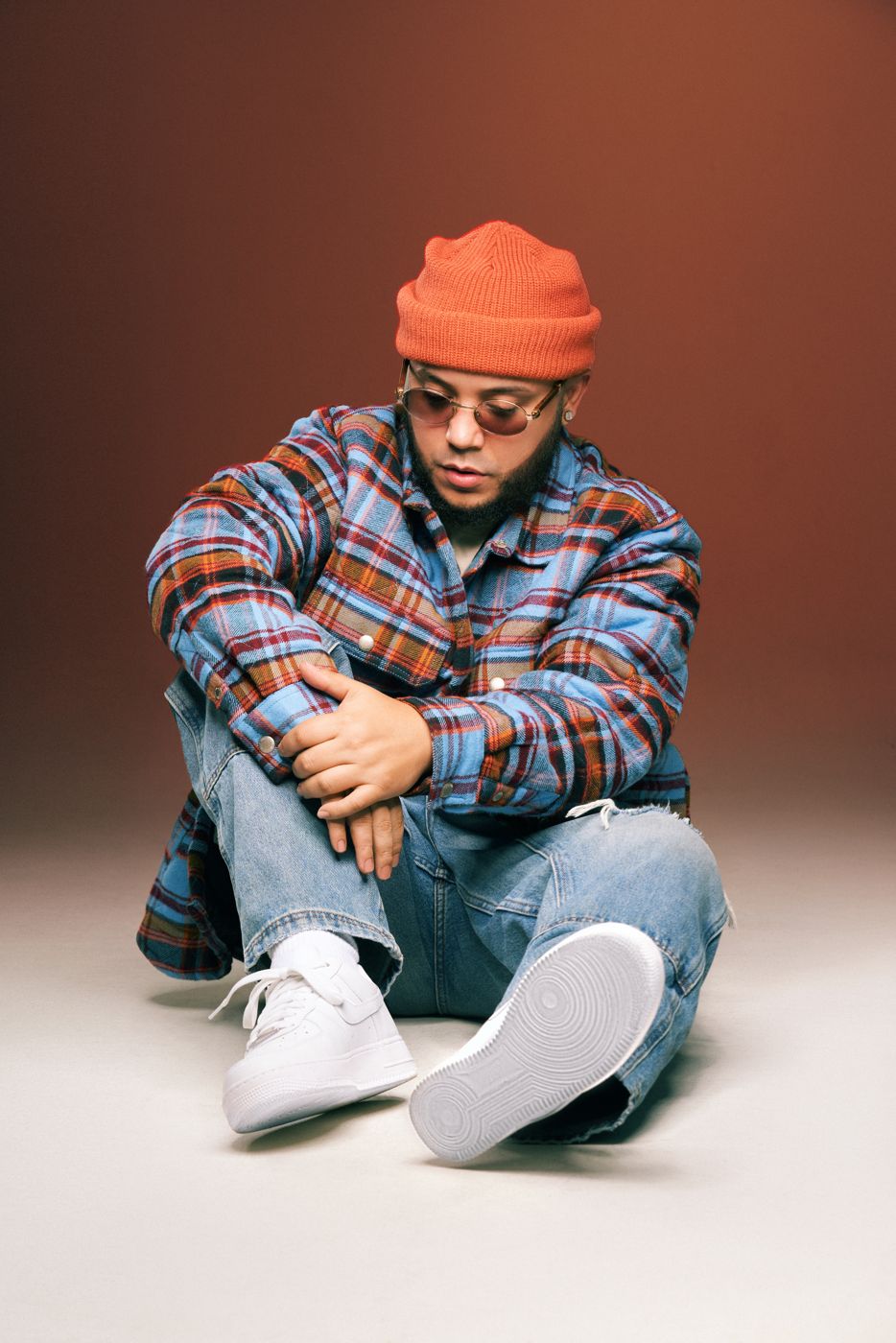 Man in a plaid jacket and orange beanie seated on the floor