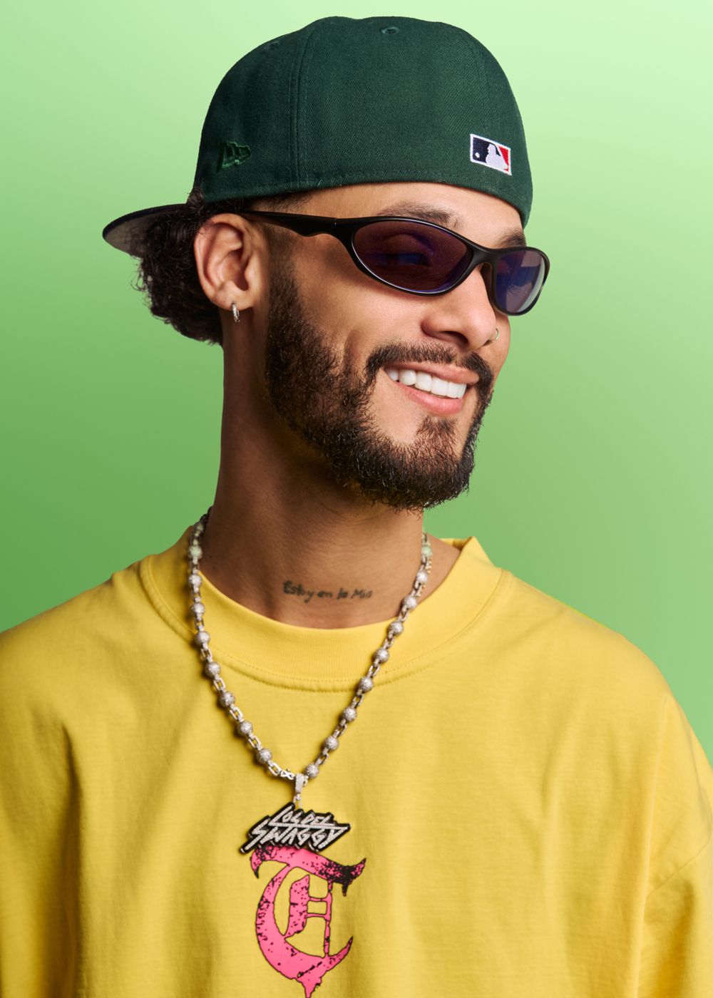 Artist in a yellow tee and green cap against a green backdrop