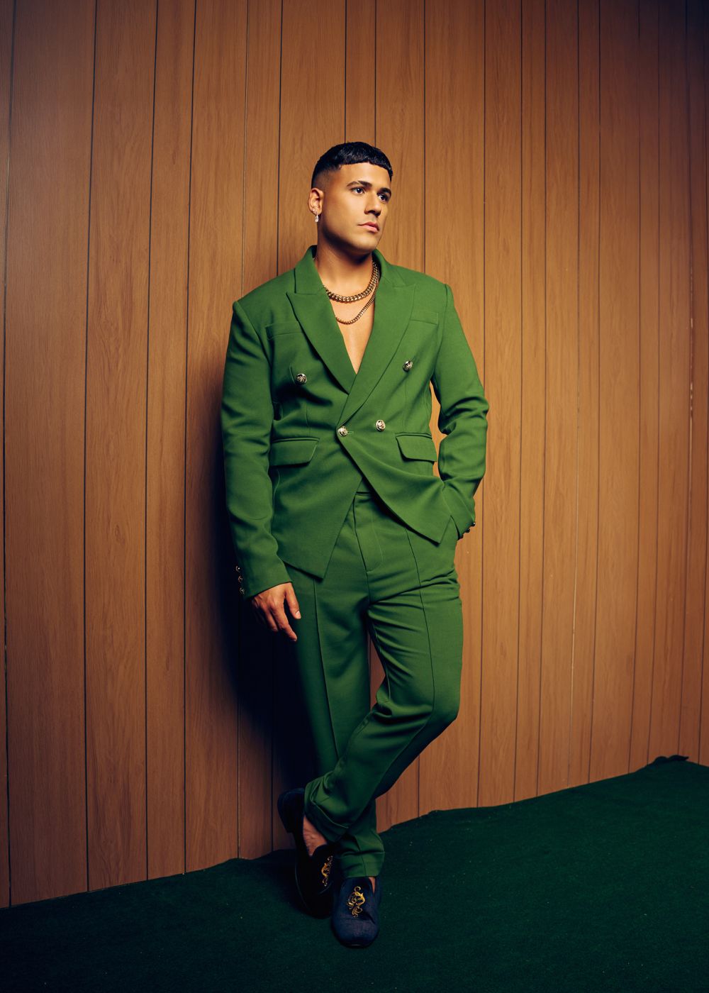Artist in a green double-breasted suit leaning on a wood-paneled wall