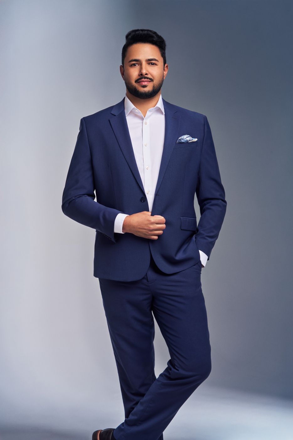 Man in a navy suit standing with hands together