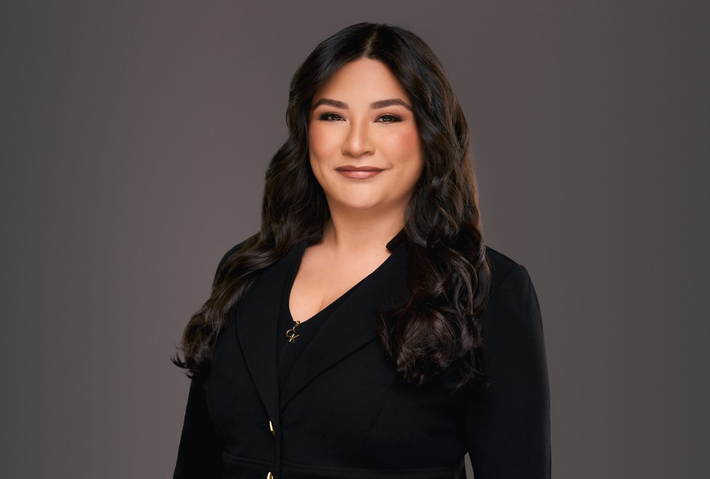 Attorney headshot in a black blazer on a charcoal backdrop